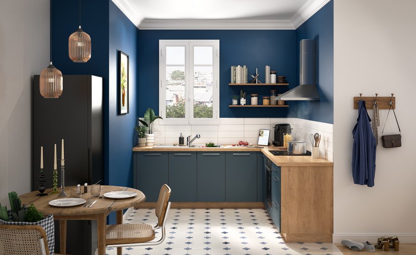 Cuisine en L bleu alby avec plan de travail et éléments en bois clair, étagères murales, et sol en carreaux de ciment à motifs bleus.