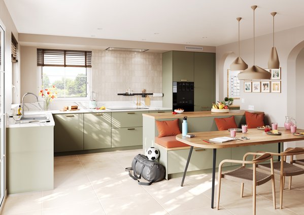 Cuisine familiale vert olive avec coin banquette intégré Grande cuisine ouverte vert olive, îlot central intégrant un coin repas avec banquette et coussins orange, crédence carrelée beige texturée et suspensions originales.
